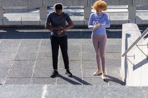 African american friends checking smartwatches during outdoor workout on urban terrace