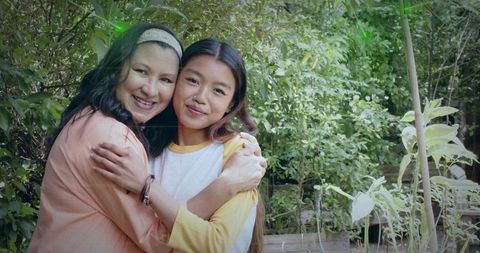 Hugging mother and daughter in backyard garden with raised beds, smiling and warm family bond