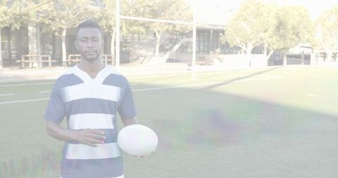 Rugby player in striped jersey holding ball on sunlit pitch with goalposts and copy space