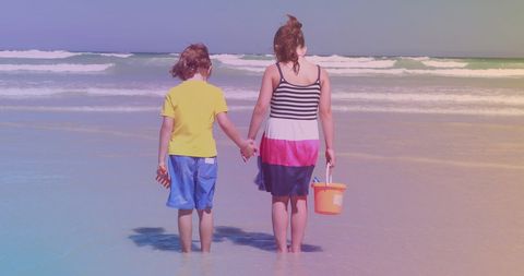 Siblings holding hands at sunny beach enjoying summer