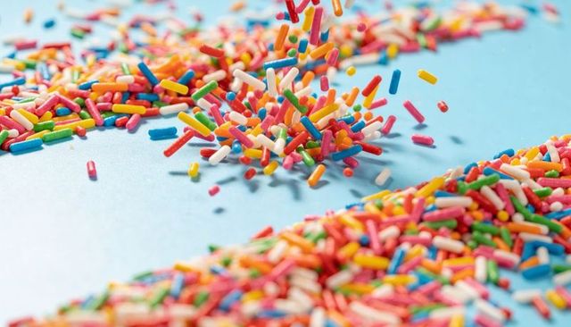Falling multicolor sprinkles forming mound on pastel blue surface, macro candy texture