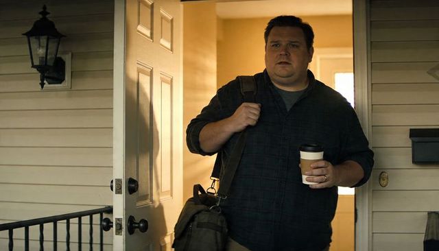 Morning commuter leaving home holding takeaway coffee carrying duffel bag through doorway