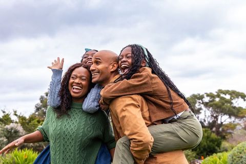 Joyful african american family enjoying piggyback fun in park during cloudy day