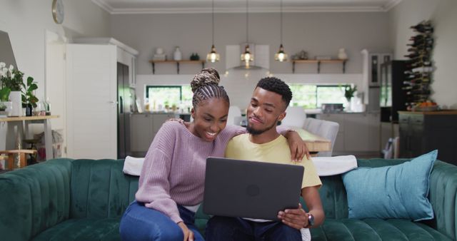 Young couple enjoying time together on comfortable sofa in modern living room, using laptop. Scene depicts a cozy environment, perfect for articles or advertisements related to technology, relationship bonding, home decor, or remote work.