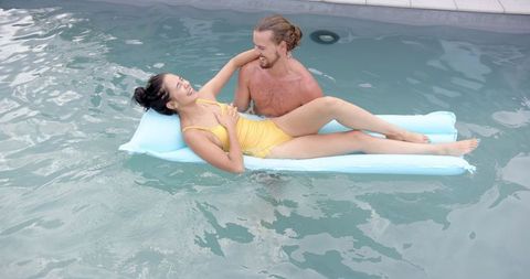 Joyful couple relaxing in swimming pool on light blue float