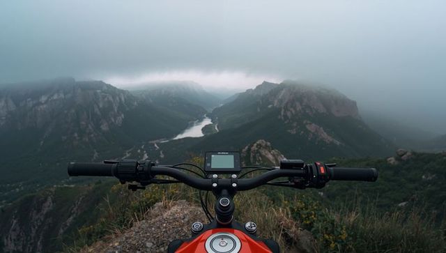 Red motorcycle handlebars overlooking misty mountain valley with winding river and cliffs