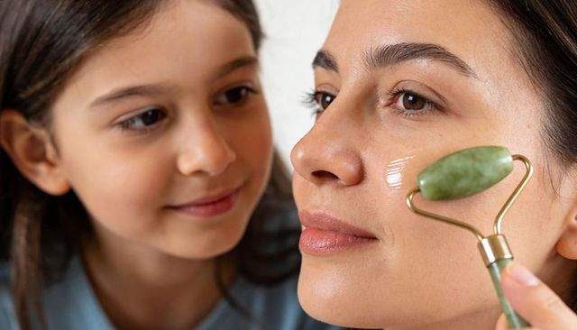 Mother using jade roller while daughter watching closeup skincare routine at home