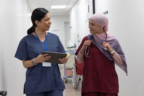 Diverse nurses walking and collaborating in hospital corridor with tablet