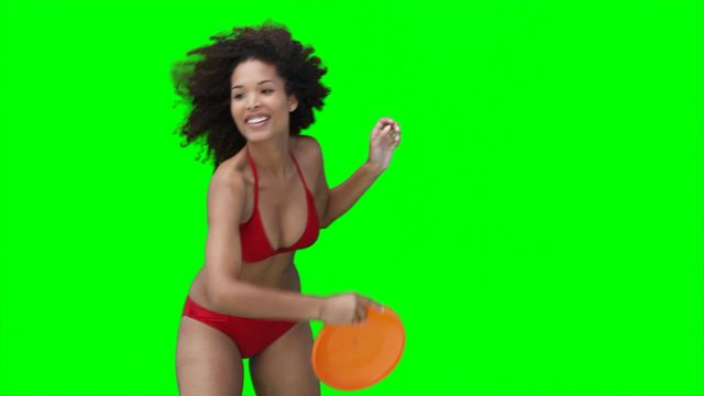 Woman in red swimwear joyfully throwing frisbee against bright green background. Ideal for summer-themed advertisements, recreational activities promotions, or green screen video editing elements depicting outdoor fun.