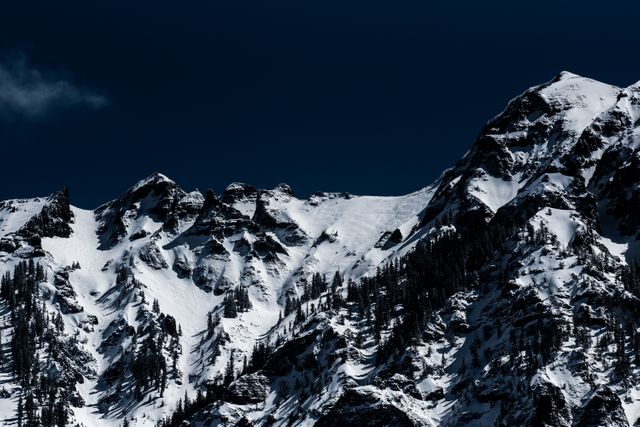 Dramatic snow-covered mountain peaks silhouetted against a clear night sky. Perfect for travel brochures, inspirational posters, and winter sports promotions.