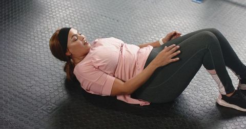 African american woman doing core crunches on gym floor wearing pink tee and fitness tracker