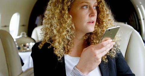 Businesswoman using smartphone on private jet interior