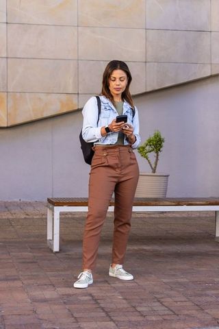 Young african woman checking smartphone at urban plaza wearing denim jacket and backpack