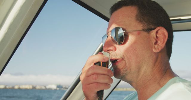 Caucasian man in sunglasses talking on radio in cabin of small boat sailing on a sunny day. Leisure, hobbies, free time, travel and vacations.