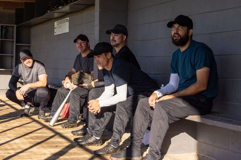 Baseball teammates sitting in dugout watching game sharing equipment and camaraderie