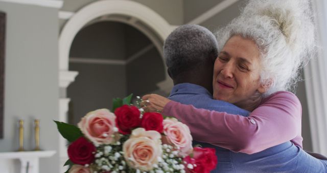 Elderly couple sharing an affectionate hug, with a beautiful bouquet of roses in hands. Perfect for illustrating love in old age, romantic gestures, or relationships among seniors. Ideal for websites, advertisements, or articles focused on family relationships, elderly care, romance, and home settings.