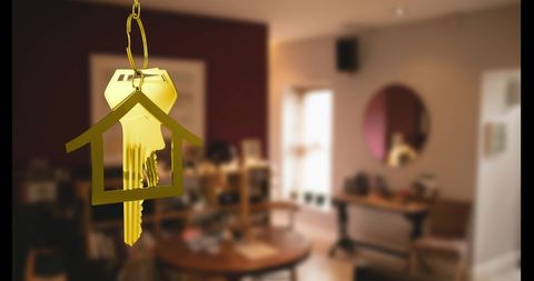 This image depicts a golden key in a house-shaped holder hanging brightly over a blurred home interior. The visual combination makes it perfect for illustrating concepts like home ownership, real estate transactions, rental opportunities, or unlocking success in home-buying markets. Ideal for marketing materials, blog posts, and editorial content focused on residential properties or moving into a new house.