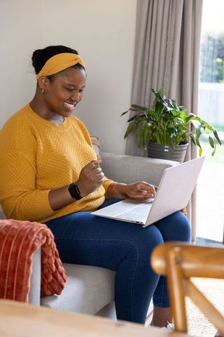 African american woman celebrating success while using laptop on cozy living room sofa