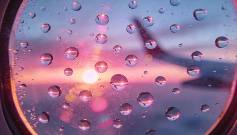 Sunset reflections through rain-dotted airplane window with wing silhouette and lensflare