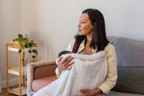 Mother cradling newborn under plush blanket on sofa, soothing calm nurturing moment