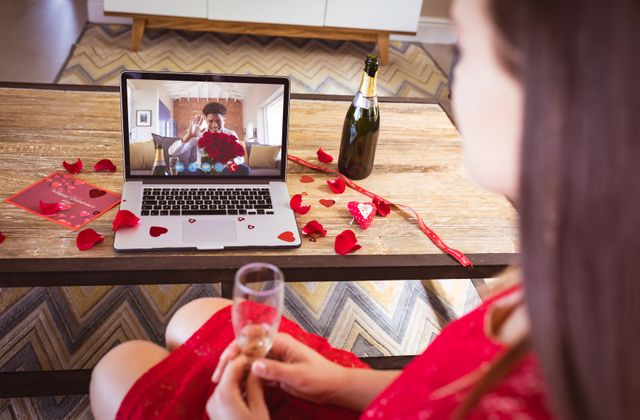 Biracial young man showing bouquet to biracial girlfriend having champagne during online dating. unaltered, online dating, video call and distant valentine day celebration.