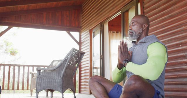 Mature man in yoga pose meditating outdoors on wooden deck of log cabin. Useful for wellness and health blogs, meditation retreats promotions, or lifestyle articles about mindfulness and outdoor activities.