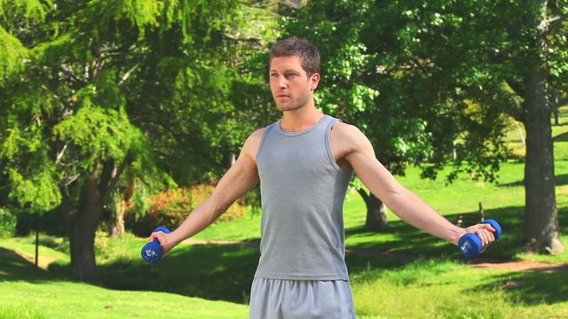 Man working out with dumbbells in a green park, promoting outdoor fitness activities. This image can be used for articles on fitness tips, workout motivation, or healthy living. Ideal for online fitness programs or lifestyle blogs.