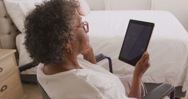 Senior african american woman sitting in wheelchair and using tablet with copy space on screen. Senior lifestyle, disability, free time, communication and domestic life.