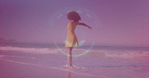 Woman standing in shallow surf wearing yellow dress showing holographic ring at sunrise