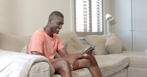 Man Relaxing on Beige Sectional Sofa Using Tablet and Smiling in Bright Modern Living Room