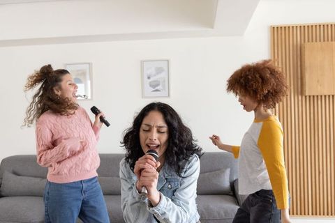 Diverse friends singing and dancing at home with handheld microphones, karaoke trio