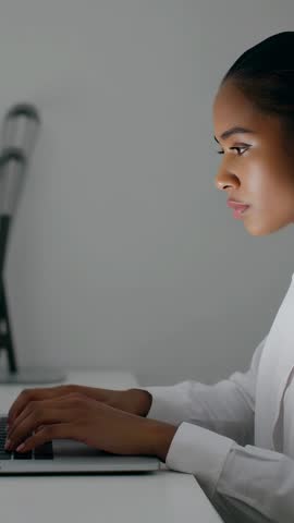 Vertical video: woman typing on laptop, working from home, concentrating in minimalist workspace
