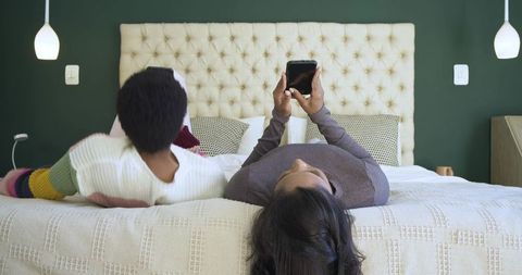 Diverse Friends Relaxing on Bed Using Tablet in Modern Bedroom