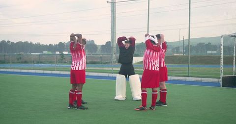Field Hockey Teammates Stretching with Goalkeeper on Turf