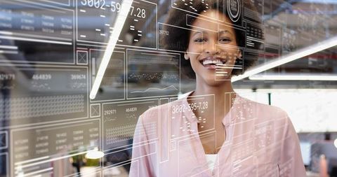 Smiling businesswoman using transparent data dashboard overlay in modern tech workspace