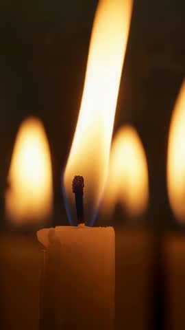 Vertical close-up of flickering candle wick with dripping wax and blurred flame bokeh