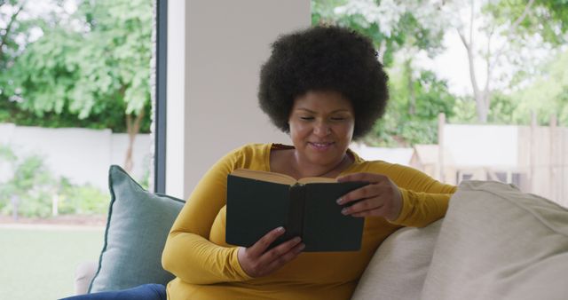 Smiling Woman Reading Book on Sofa Near Window - Download Free Stock Images Pikwizard.com