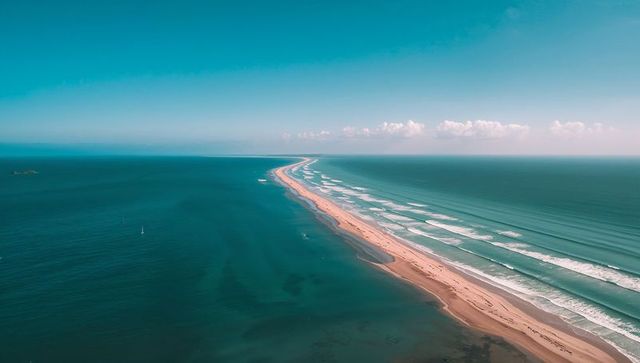 Drone capturing long sandbar stretching toward horizon across turquoise ocean with waves