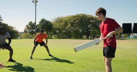 Young diverse team practicing cricket in sunny park batting and fielding training session