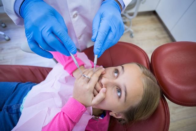 Young girl covering mouth with hands while dentist holding dental tools. Ideal for illustrating dental anxiety in children, pediatric dental care, healthcare services, and promoting dental clinics specializing in child-friendly environments.