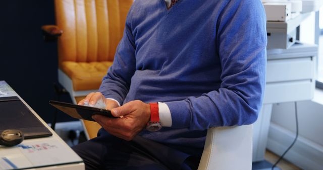 A middle-aged man in a blue sweater is seated, using a tablet, with copy space - Download Free Stock Photos Pikwizard.com