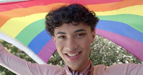 Young Man Holding Rainbow Flag in Sunny Park Celebrating Diversity