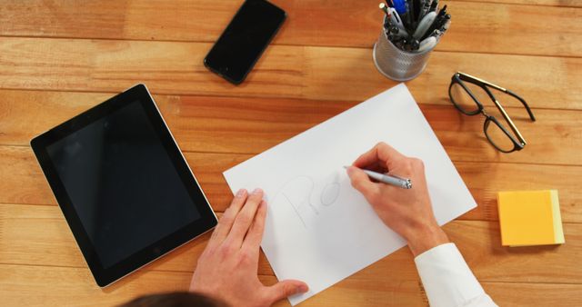 Person Writing on Paper at Wooden Desk with Tablet and Office Supplies - Download Free Stock Images Pikwizard.com