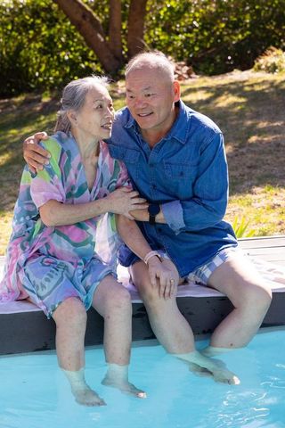 Asian senior couple enjoying sunlit poolside moment with feet in water
