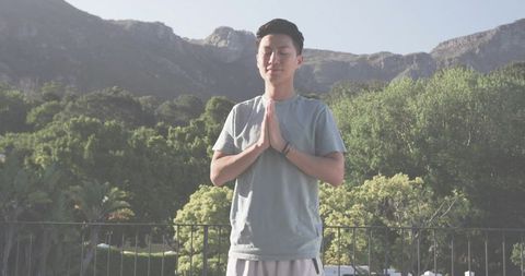Young asian man meditating on terrace with mountain backdrop, practicing mindfulness