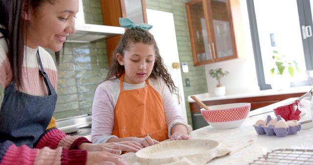 Mother and daughter are enjoying baking a pastry together in modern kitchen. Mother, wearing apron, guiding her child on how to knead dough on countertop. Bright light and cozy environment emphasize family bonding and home activities. Ideal for content related to family life, parenting, and cooking tutorials.