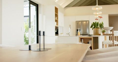 Wooden dining table anchoring bright open-plan kitchen featuring candles and island
