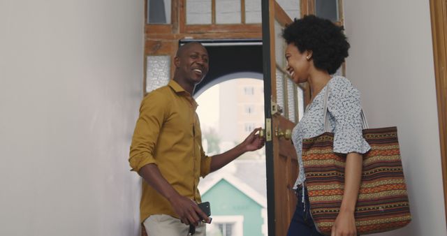 Happy african american couple with bag and smartphone talking at open front door. Relationship, free time, domestic life and lifestyle, unaltered.