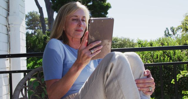 Senior caucasian woman using tablet sitting in sunny garden. staying at home in isolation during quarantine lockdown.