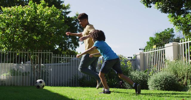 Happy biracial man and his son playing football in garden. domestic life, spending time at home.